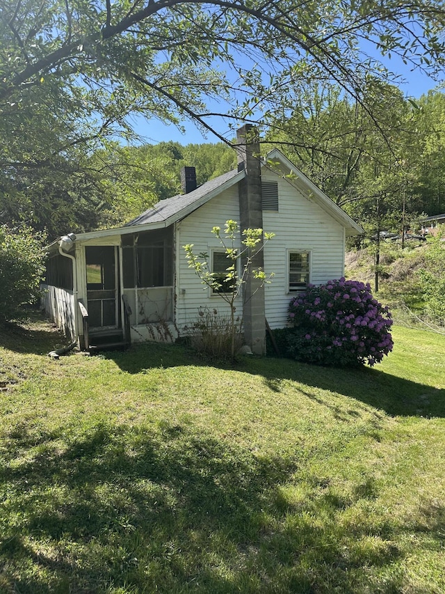 view of side of home featuring a sunroom, a lawn, and a chimney