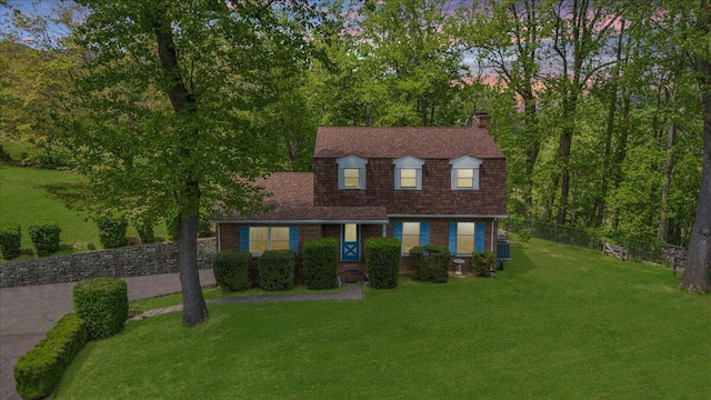 view of front facade with a chimney, roof with shingles, fence, and a front yard