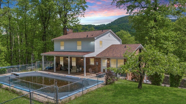 rear view of house featuring brick siding, an outdoor living space with a fire pit, fence, and a chimney