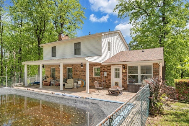 back of property with a fenced backyard, a chimney, a fire pit, and brick siding