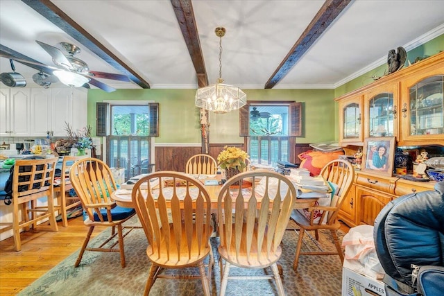dining room featuring wainscoting, beam ceiling, wooden walls, light wood-style floors, and ornamental molding