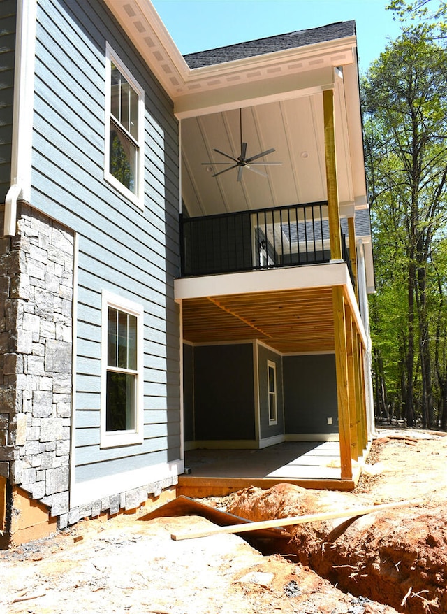 exterior space with ceiling fan, stone siding, and a balcony