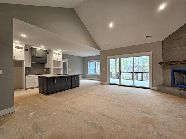 kitchen with high vaulted ceiling, a center island with sink, white cabinetry, baseboards, and open floor plan