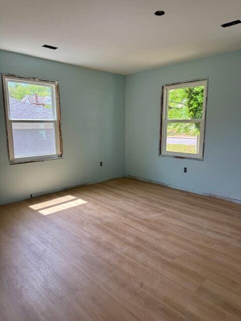 unfurnished room with visible vents, wood finished floors, and plenty of natural light
