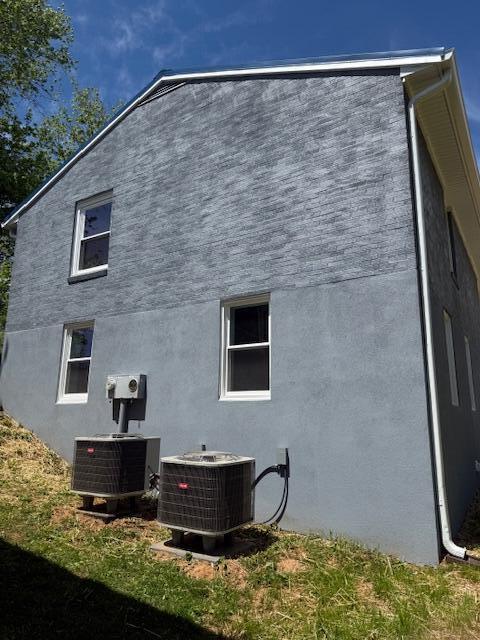 back of house with stucco siding and central AC unit