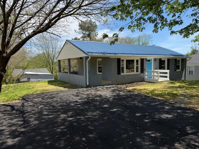 view of front of house featuring stucco siding, a standing seam roof, metal roof, driveway, and a front yard