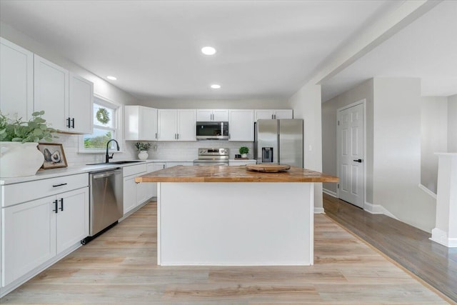 kitchen featuring a sink, stainless steel appliances, white cabinetry, decorative backsplash, and a kitchen island