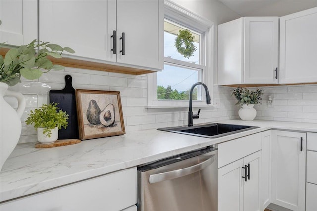 kitchen featuring backsplash, stainless steel dishwasher, a sink, light stone counters, and white cabinetry