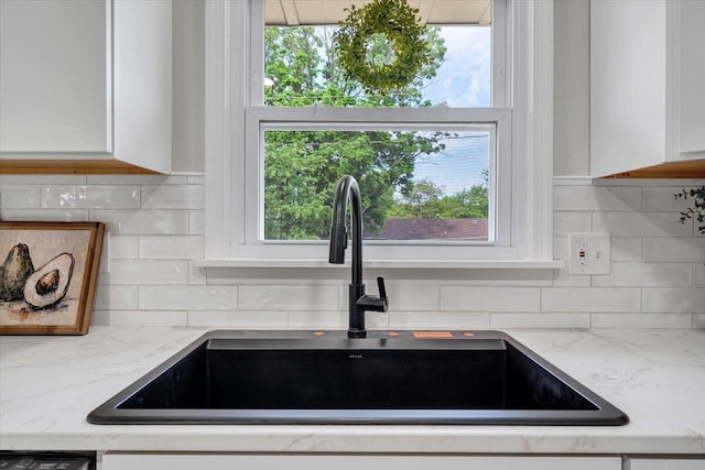 interior details featuring backsplash, white cabinetry, light stone countertops, and a sink