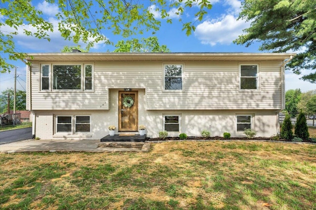 split foyer home with a patio area, a front lawn, and brick siding