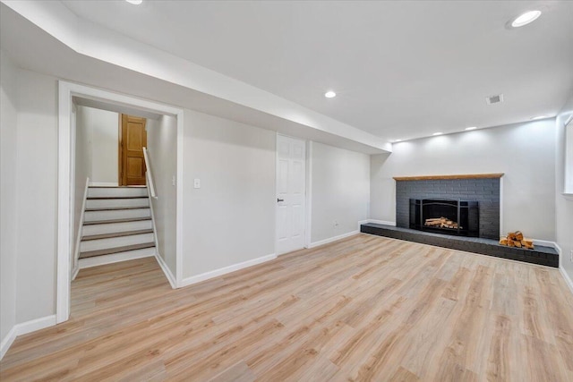 unfurnished living room with baseboards, a brick fireplace, wood finished floors, and visible vents
