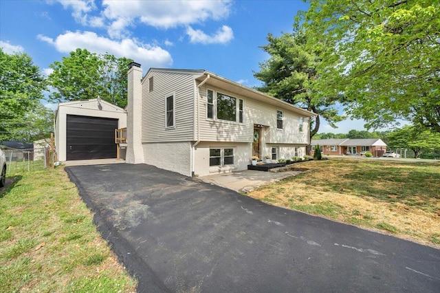 raised ranch with driveway, a chimney, a garage, brick siding, and an outdoor structure