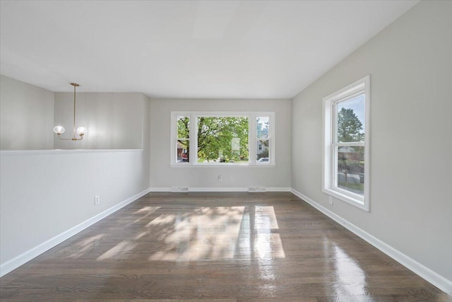 empty room featuring baseboards, dark wood finished floors, and a notable chandelier