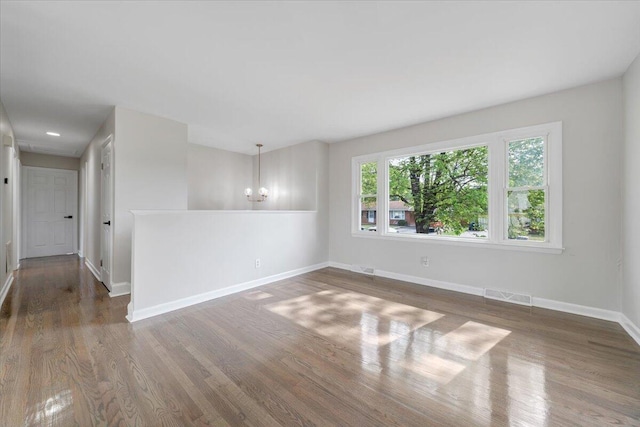 empty room featuring a chandelier, baseboards, visible vents, and wood finished floors