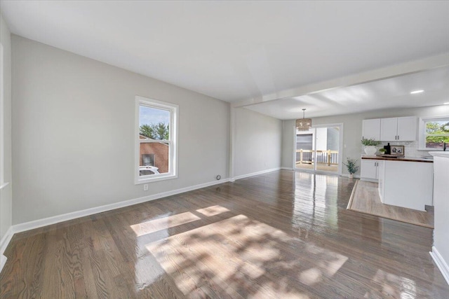 unfurnished living room featuring baseboards, wood finished floors, and a chandelier