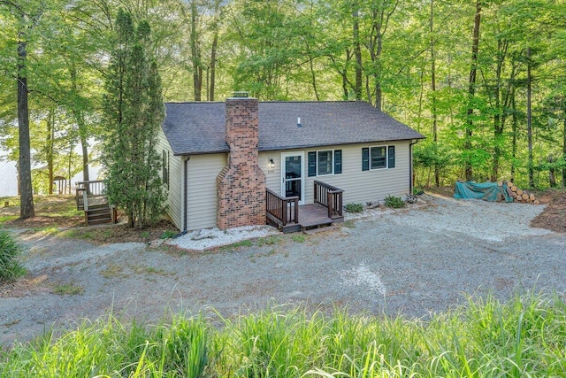 back of house with a wooden deck, a shingled roof, and a chimney