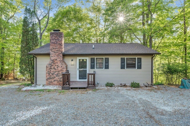 back of property with a shingled roof and a chimney