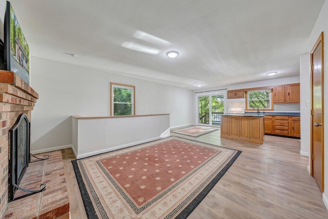 kitchen featuring a brick fireplace, baseboards, brown cabinetry, and light wood-style flooring