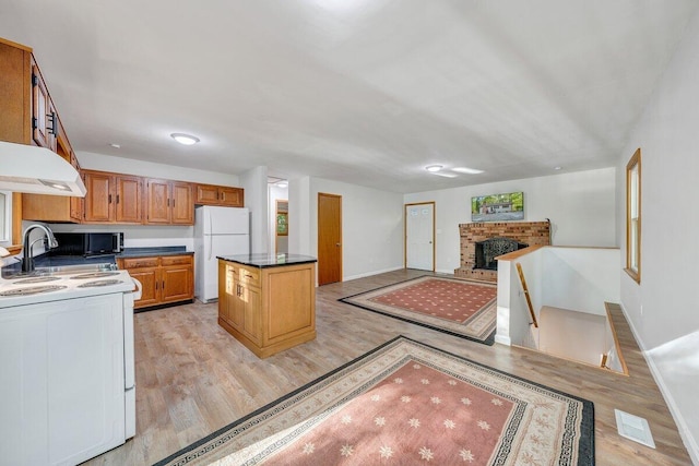 kitchen featuring freestanding refrigerator, black microwave, light wood-type flooring, under cabinet range hood, and range