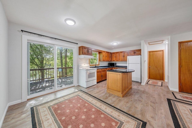 kitchen featuring a sink, baseboards, under cabinet range hood, white appliances, and light wood-style flooring
