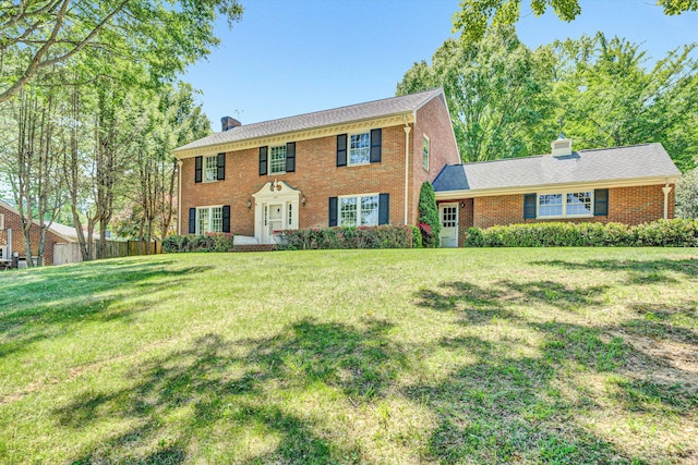 colonial home featuring brick siding, a front yard, and a chimney