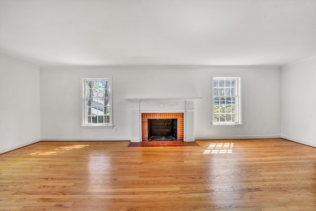 unfurnished living room featuring plenty of natural light, a brick fireplace, and wood finished floors