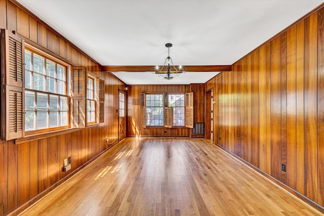 unfurnished room featuring wooden walls, baseboards, wood finished floors, and a notable chandelier