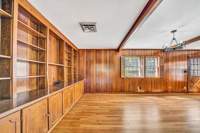 empty room with visible vents, wood walls, light wood-type flooring, beam ceiling, and a notable chandelier