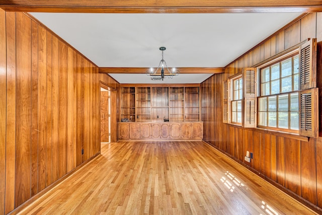 empty room with wooden walls, a notable chandelier, beam ceiling, wood-type flooring, and built in features