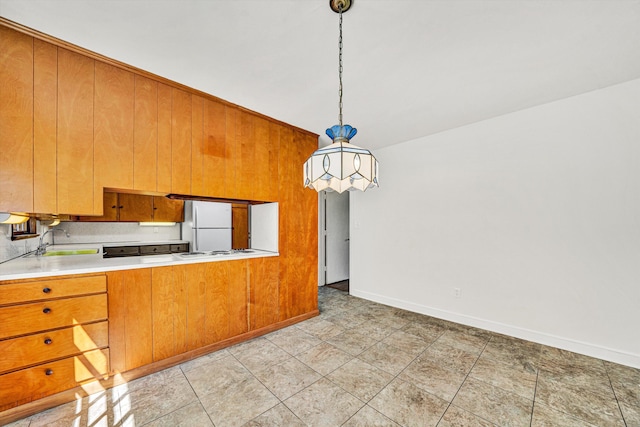 kitchen featuring a sink, baseboards, freestanding refrigerator, and brown cabinets