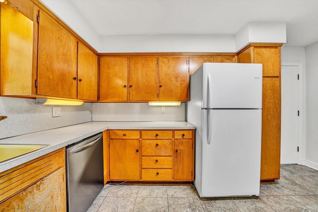 kitchen featuring freestanding refrigerator, stainless steel dishwasher, brown cabinetry, and light countertops