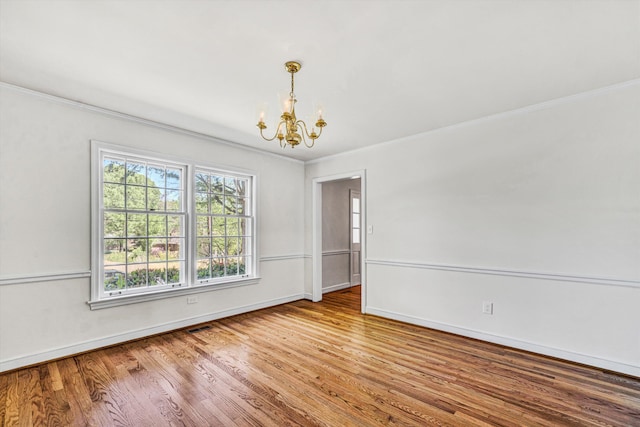 empty room with an inviting chandelier, crown molding, visible vents, wood finished floors, and baseboards