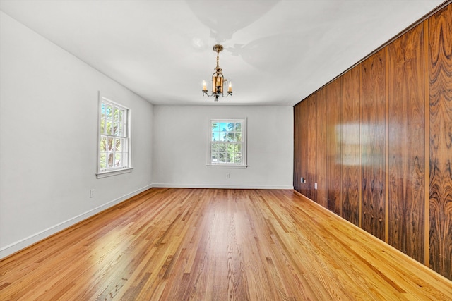 spare room featuring baseboards, an inviting chandelier, and light wood-type flooring