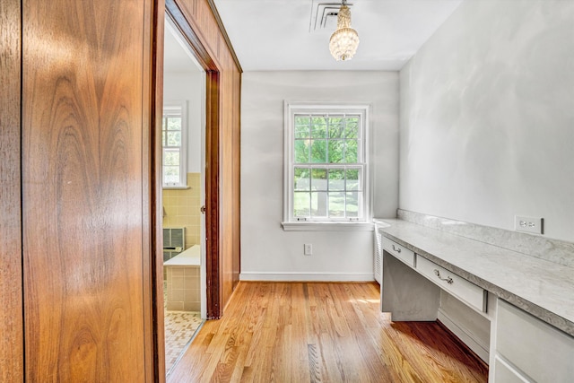unfurnished office featuring light wood-style floors, baseboards, built in study area, and visible vents
