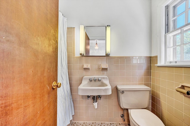 bathroom with a sink, toilet, a wainscoted wall, tile walls, and curtained shower