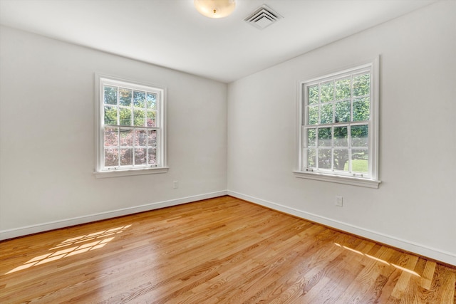 empty room with baseboards, plenty of natural light, wood finished floors, and visible vents