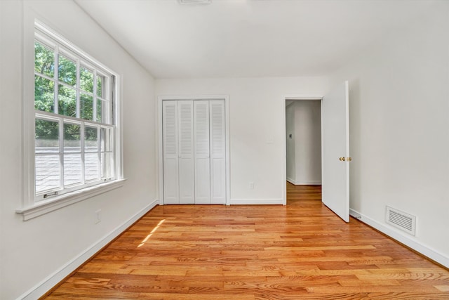 unfurnished bedroom with visible vents, light wood-style floors, baseboards, and a closet