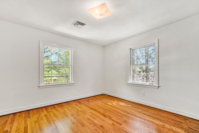 empty room with baseboards, light wood finished floors, and visible vents