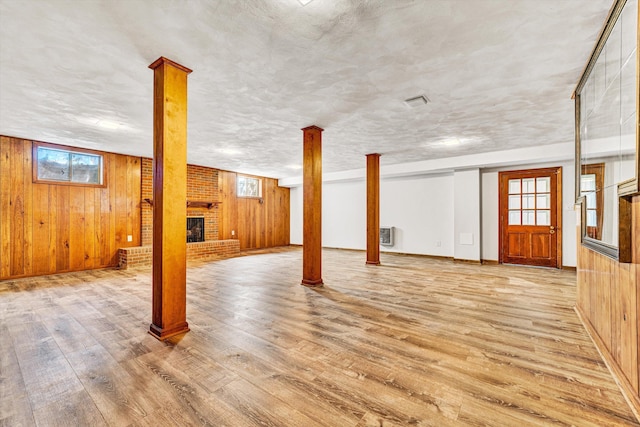 basement featuring light wood-type flooring, baseboards, a brick fireplace, and wooden walls