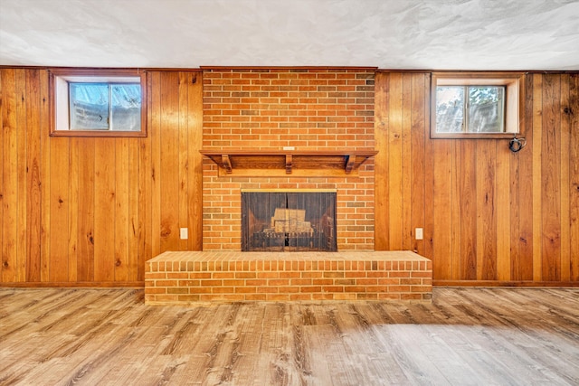 unfurnished living room with baseboards, a brick fireplace, wood finished floors, and wooden walls