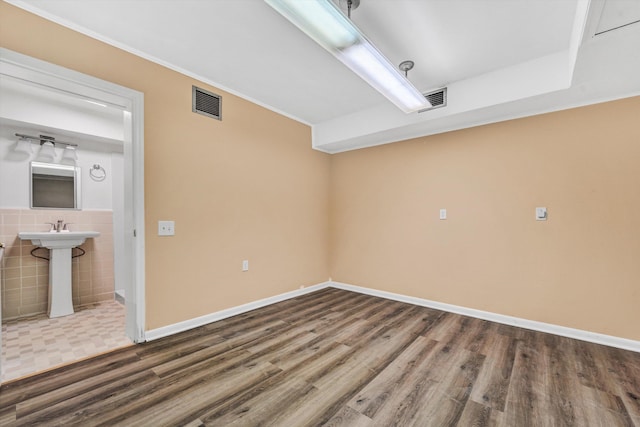 empty room featuring baseboards, a sink, visible vents, and wood finished floors