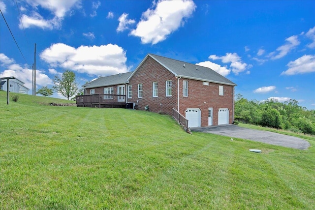 back of property featuring aphalt driveway, a lawn, a deck, brick siding, and an attached garage