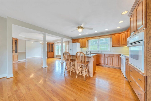kitchen featuring ceiling fan, white appliances, light countertops, decorative columns, and a kitchen bar