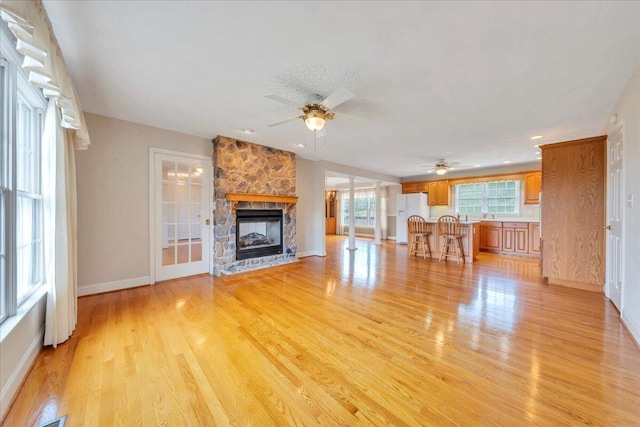 unfurnished living room with baseboards, a ceiling fan, light wood-style flooring, and a fireplace