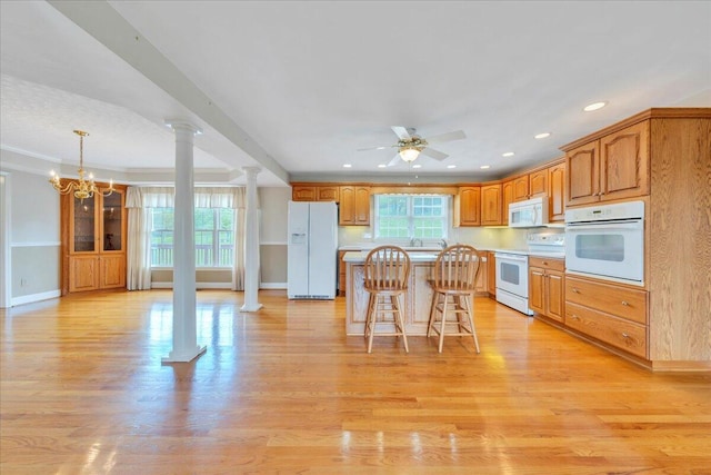 kitchen with white appliances, a kitchen breakfast bar, ceiling fan with notable chandelier, a center island, and ornate columns