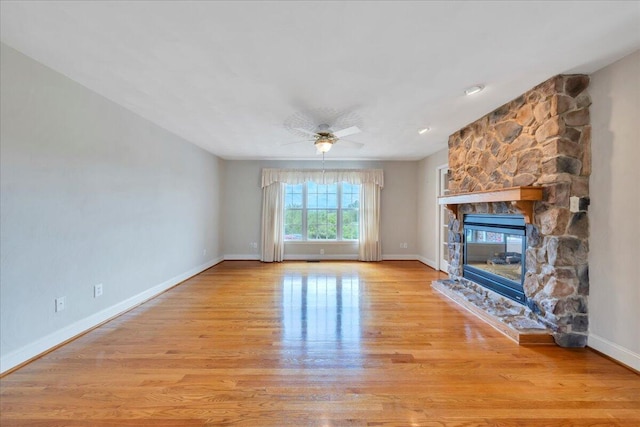 unfurnished living room featuring light wood-type flooring, a ceiling fan, baseboards, and a stone fireplace
