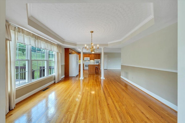 unfurnished dining area featuring a notable chandelier, light wood-type flooring, a tray ceiling, visible vents, and ornamental molding