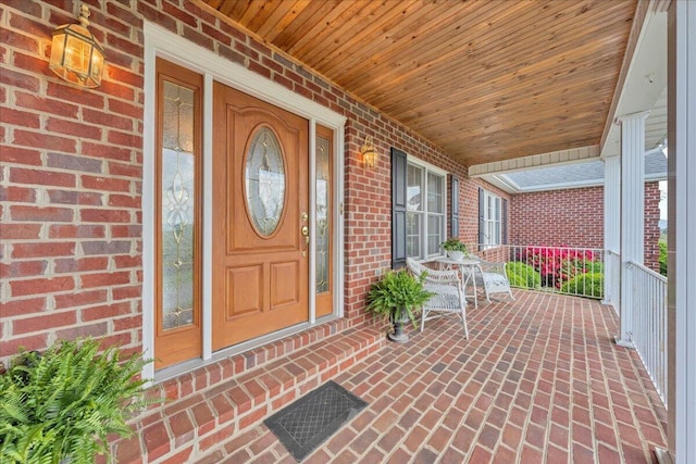 view of exterior entry featuring brick siding and covered porch