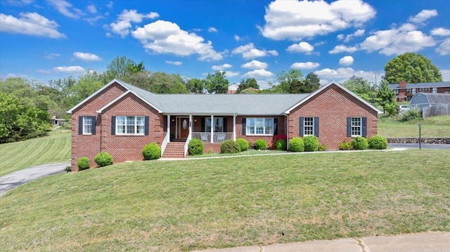 ranch-style house featuring a porch, a chimney, a front yard, and brick siding