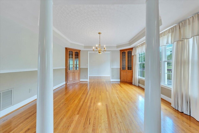 unfurnished dining area featuring decorative columns, a textured ceiling, visible vents, light wood finished floors, and a notable chandelier